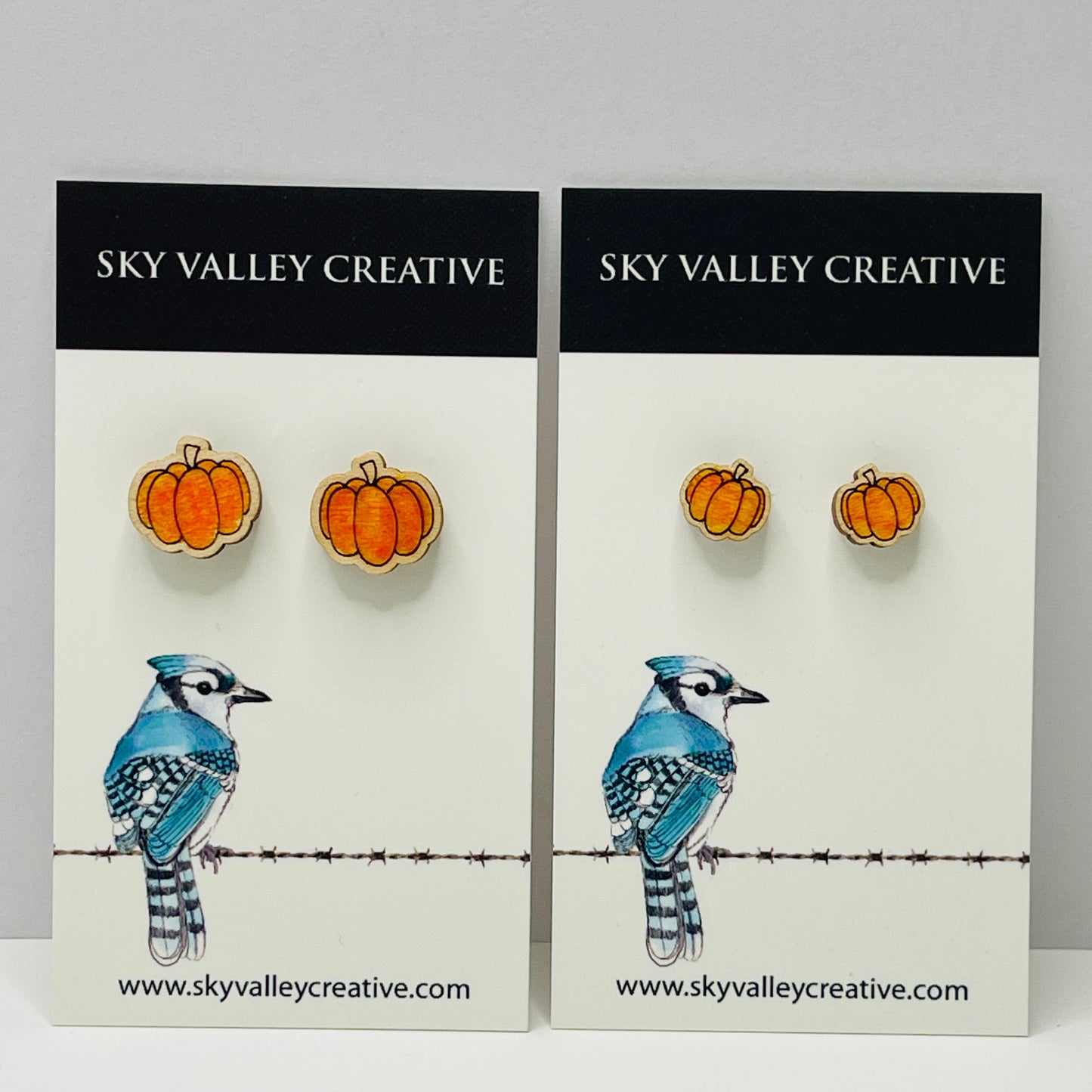 Two pairs of pumpkin post earrings on display cards with 'Sky Valley Creative' branding. Regular and small size shown.