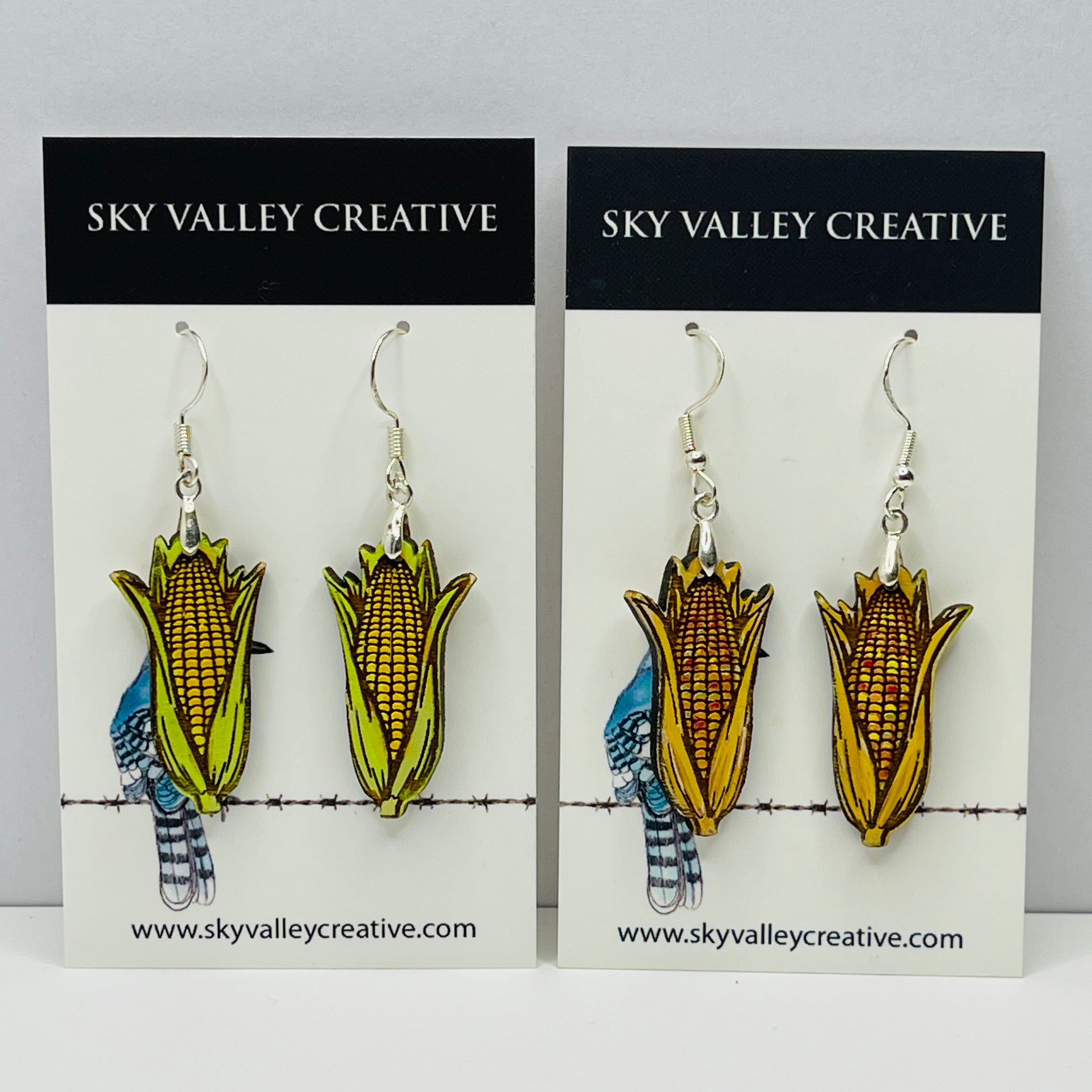 Corn on the cob and Indian corn earrings cut from maple on display cards with 'Sky Valley Creative' branding.