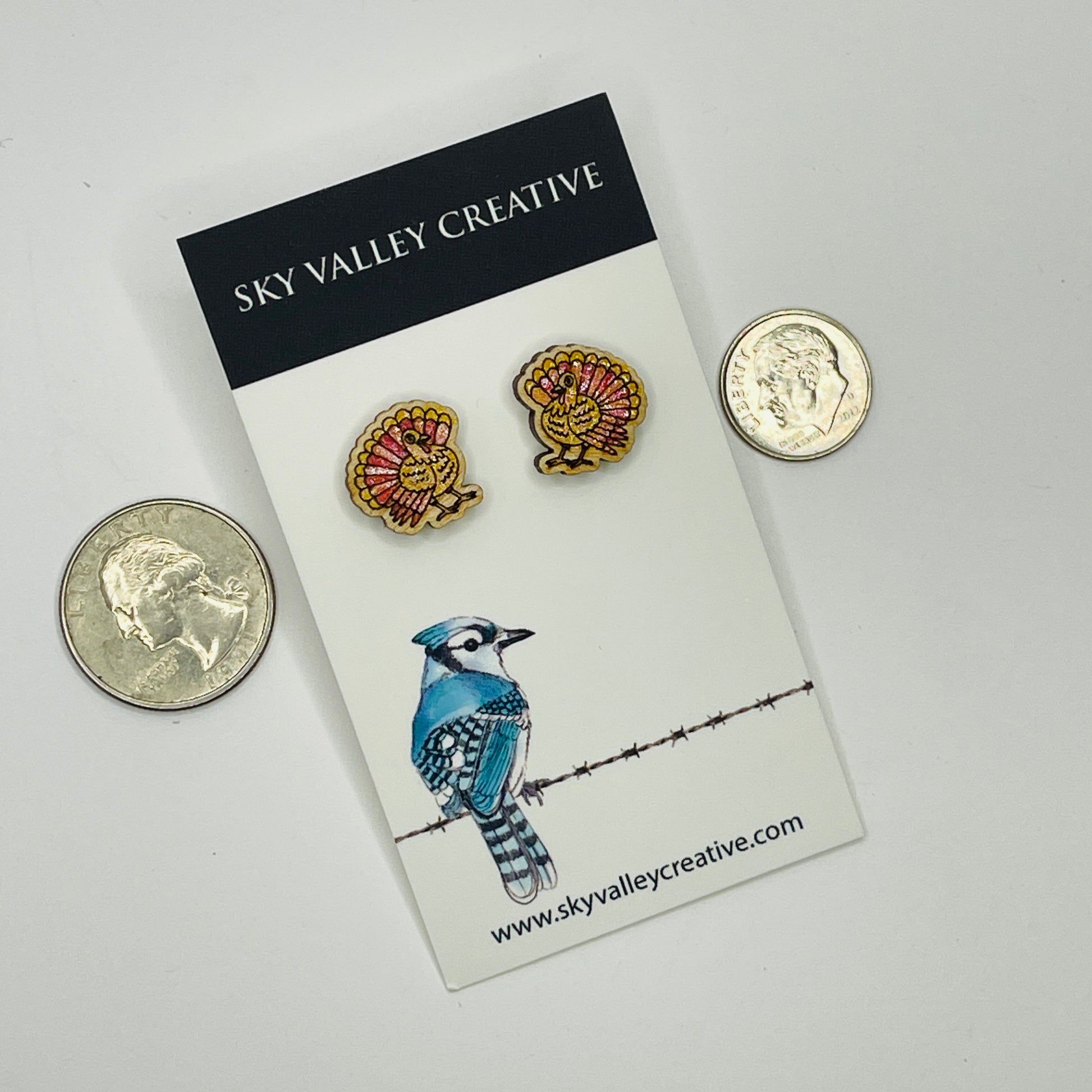 Two small turkeys hand-painted on a card with 'Sky Valley Creative' branding, next to two coins for scale.