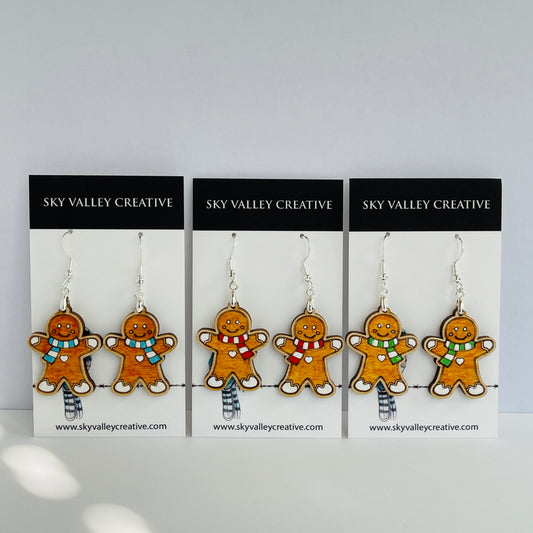 Three pairs of gingerbread man earrings with blue, red and green scarf choices on display cards with 'Sky Valley Creative' branding.